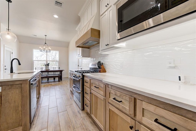 kitchen with premium range hood, sink, hanging light fixtures, appliances with stainless steel finishes, and backsplash