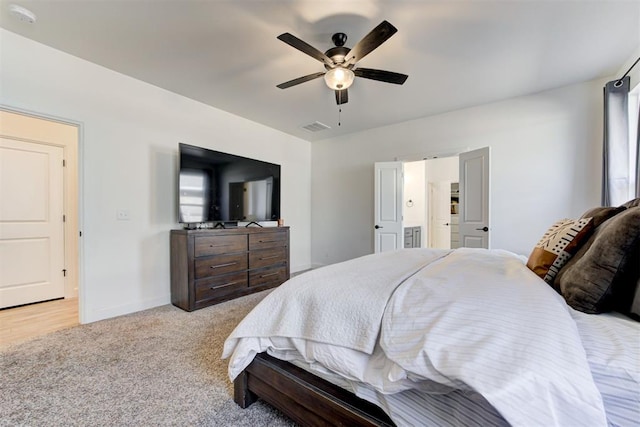 bedroom featuring light colored carpet, ceiling fan, and ensuite bath