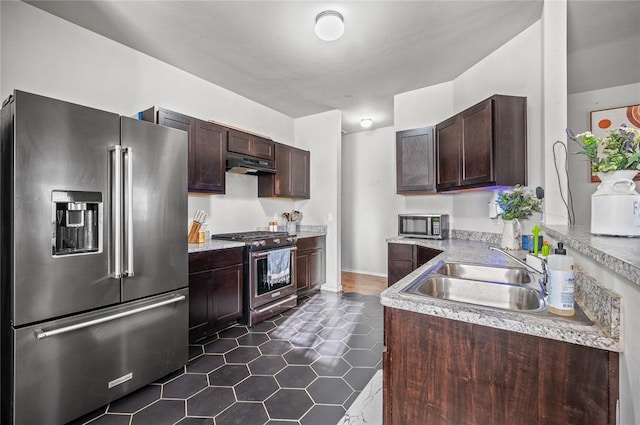 kitchen with premium appliances, dark brown cabinets, sink, and dark tile patterned flooring