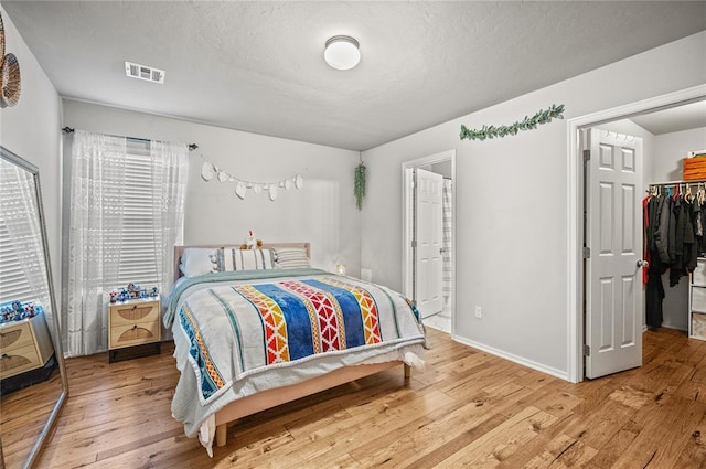 bedroom featuring ensuite bathroom, a spacious closet, a textured ceiling, a closet, and light hardwood / wood-style floors