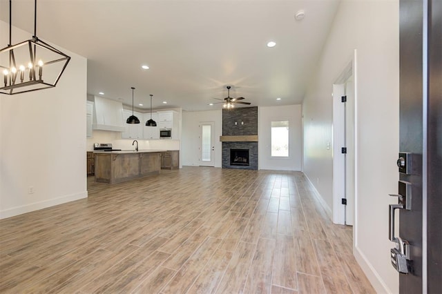 unfurnished living room featuring sink, ceiling fan with notable chandelier, a large fireplace, and light hardwood / wood-style floors