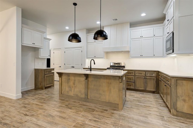 kitchen featuring stainless steel appliances, white cabinetry, sink, and a kitchen island with sink