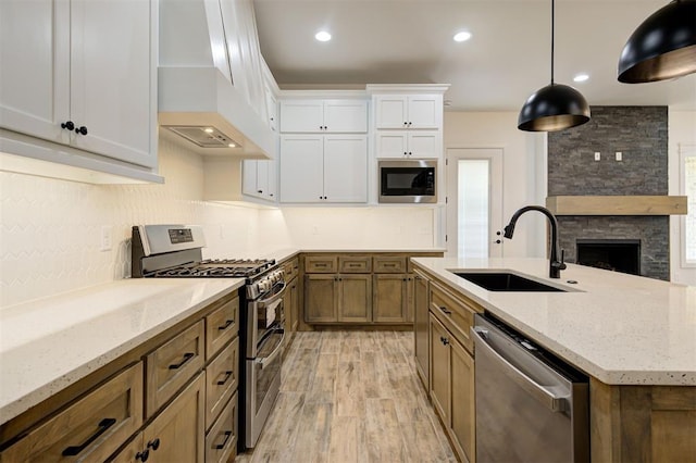 kitchen featuring sink, appliances with stainless steel finishes, white cabinetry, hanging light fixtures, and custom range hood