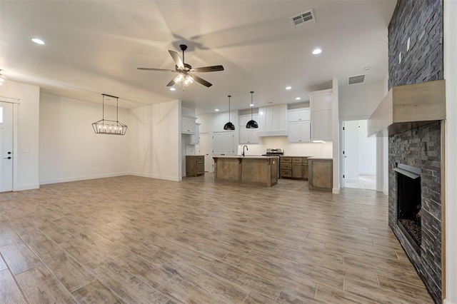 unfurnished living room with ceiling fan, sink, a fireplace, and light hardwood / wood-style floors