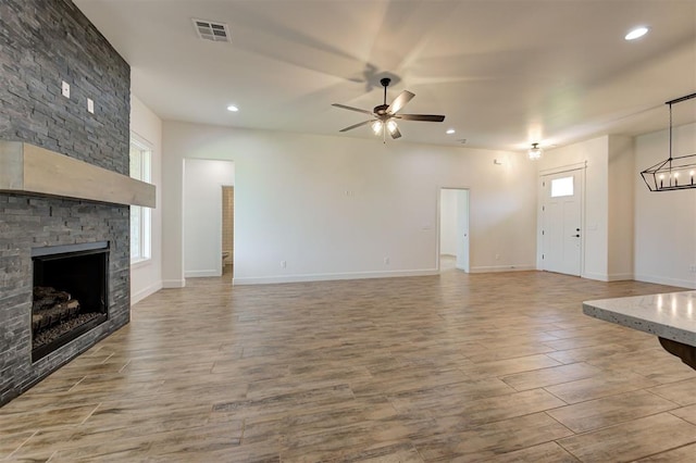 unfurnished living room featuring plenty of natural light, a fireplace, ceiling fan with notable chandelier, and light wood-type flooring