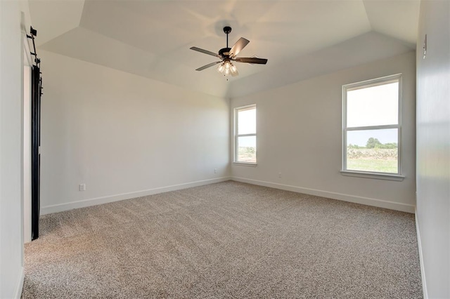 empty room with ceiling fan, a raised ceiling, vaulted ceiling, and light carpet