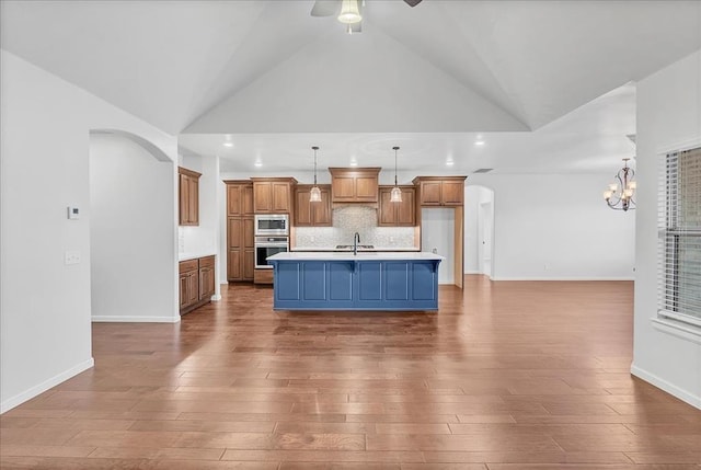 kitchen with sink, hardwood / wood-style flooring, stainless steel microwave, an island with sink, and pendant lighting