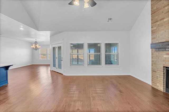 unfurnished living room with lofted ceiling, hardwood / wood-style floors, ceiling fan with notable chandelier, and a fireplace