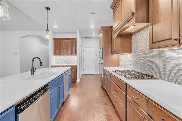 kitchen with sink, backsplash, hanging light fixtures, stainless steel appliances, and light hardwood / wood-style floors