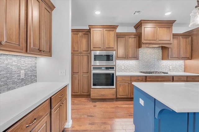 kitchen featuring hanging light fixtures, decorative backsplash, light hardwood / wood-style flooring, and stainless steel appliances