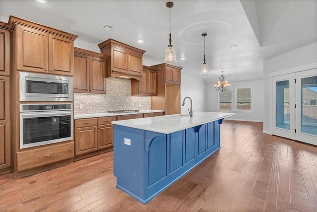 kitchen with pendant lighting, sink, a kitchen island with sink, stainless steel appliances, and light wood-type flooring