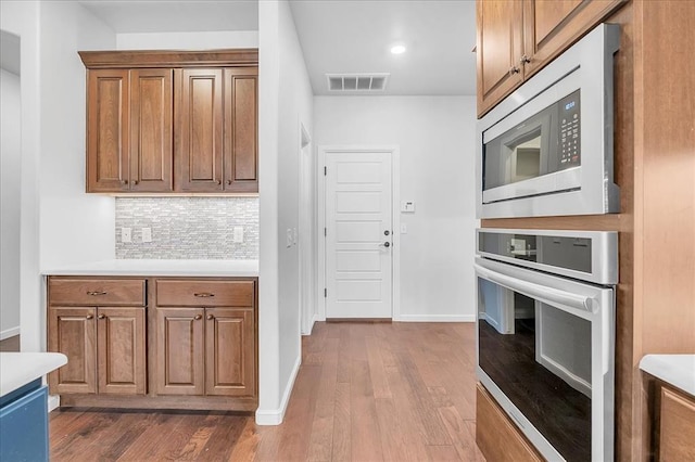 kitchen with stainless steel microwave, backsplash, hardwood / wood-style floors, and oven