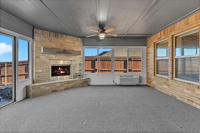 unfurnished sunroom with an outdoor brick fireplace, an AC wall unit, a healthy amount of sunlight, and ceiling fan