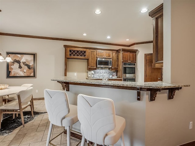 kitchen featuring light stone counters, appliances with stainless steel finishes, a kitchen bar, and backsplash