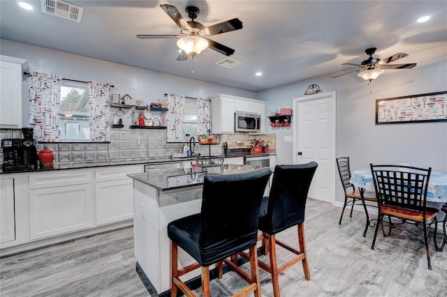 kitchen featuring a breakfast bar area, appliances with stainless steel finishes, white cabinetry, a kitchen island, and dark stone counters