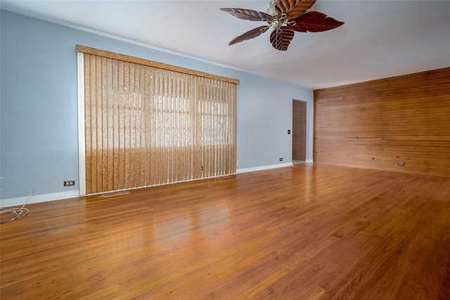 empty room featuring hardwood / wood-style flooring, wooden walls, and ceiling fan