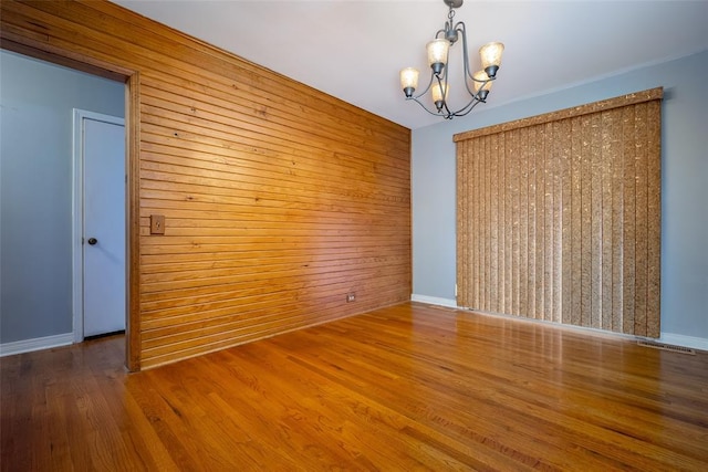 spare room featuring wooden walls, hardwood / wood-style floors, and a chandelier