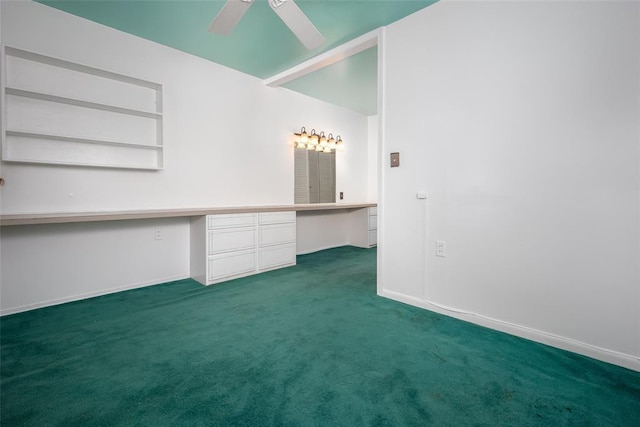 unfurnished room featuring dark colored carpet, built in desk, and ceiling fan