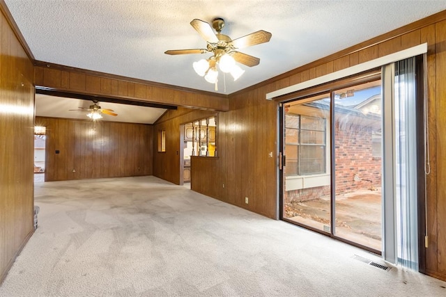 spare room with ceiling fan, light colored carpet, a textured ceiling, and wood walls