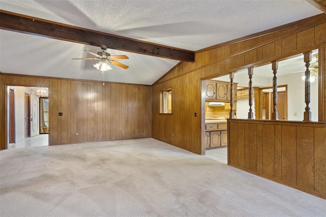 spare room with vaulted ceiling with beams, light colored carpet, a textured ceiling, and wood walls