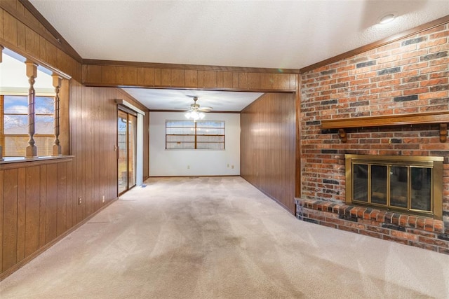 unfurnished living room with wood walls, crown molding, light carpet, ceiling fan, and a fireplace