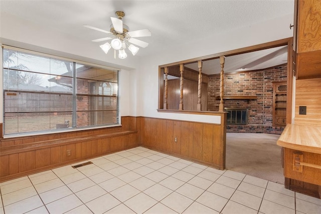 interior space with a fireplace, wood walls, light colored carpet, ceiling fan, and a textured ceiling