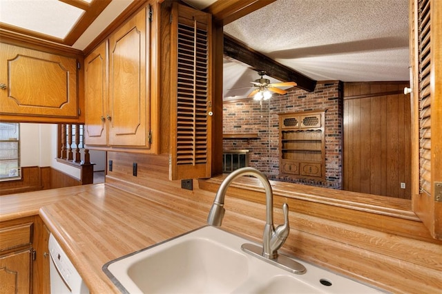 kitchen with wooden walls, lofted ceiling with beams, sink, ceiling fan, and a textured ceiling