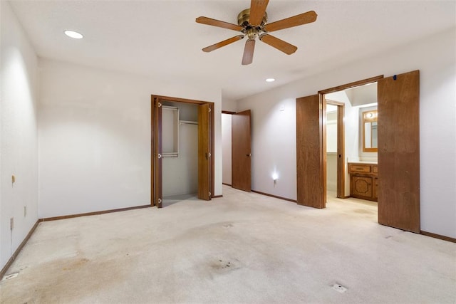 unfurnished bedroom featuring ceiling fan, light colored carpet, and ensuite bath