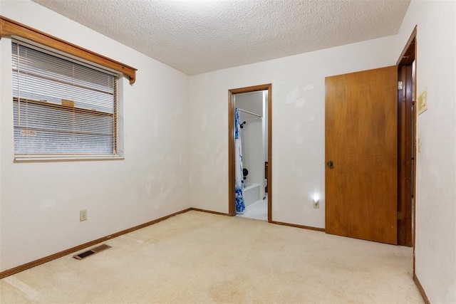 unfurnished bedroom featuring ensuite bathroom, light colored carpet, and a textured ceiling