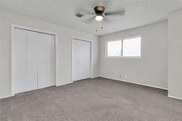 unfurnished bedroom with ceiling fan, a textured ceiling, multiple closets, and carpet flooring