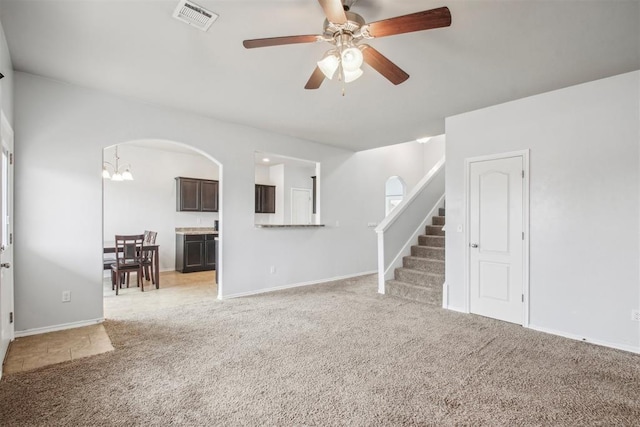 unfurnished living room featuring ceiling fan with notable chandelier and light carpet