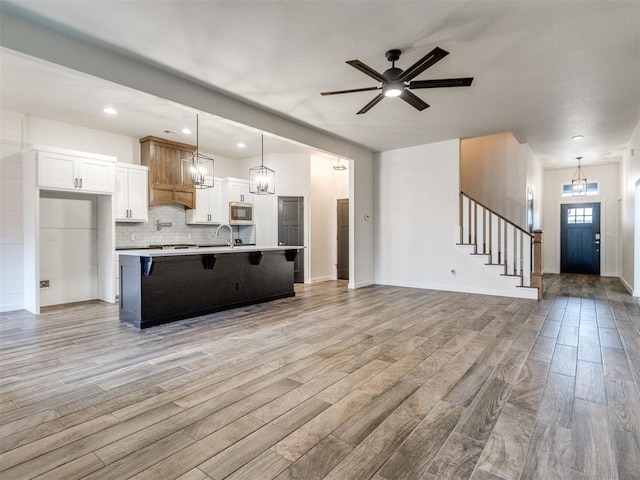 kitchen with a breakfast bar, pendant lighting, white cabinets, backsplash, and a large island with sink