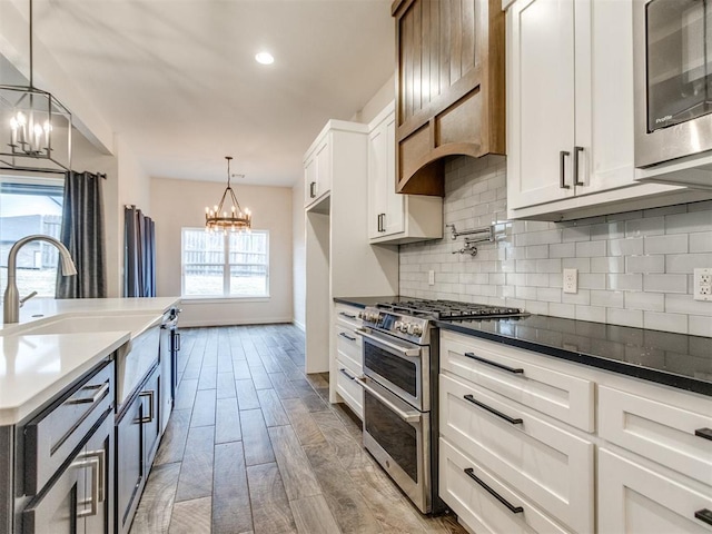 kitchen with an inviting chandelier, hanging light fixtures, stainless steel appliances, decorative backsplash, and white cabinets