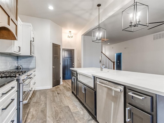 kitchen featuring sink, stainless steel appliances, tasteful backsplash, white cabinets, and decorative light fixtures