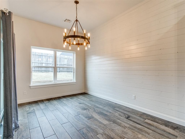 empty room with wood-type flooring and a notable chandelier