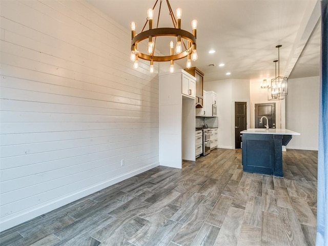 kitchen featuring white cabinetry, a chandelier, hanging light fixtures, a center island with sink, and range with two ovens