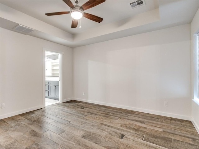 spare room featuring a raised ceiling, ceiling fan, and light wood-type flooring