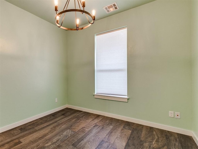 spare room featuring a notable chandelier and dark wood-type flooring