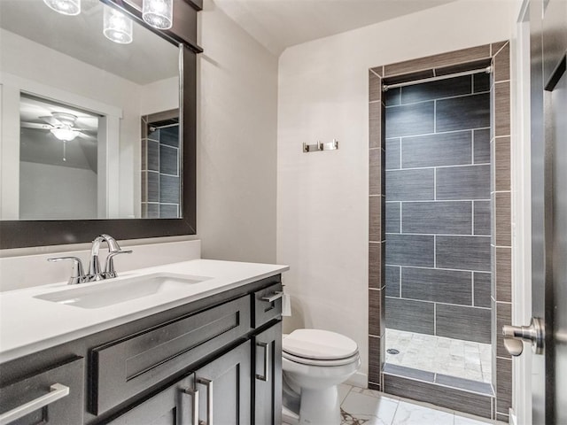 bathroom with ceiling fan, tiled shower, vanity, and toilet