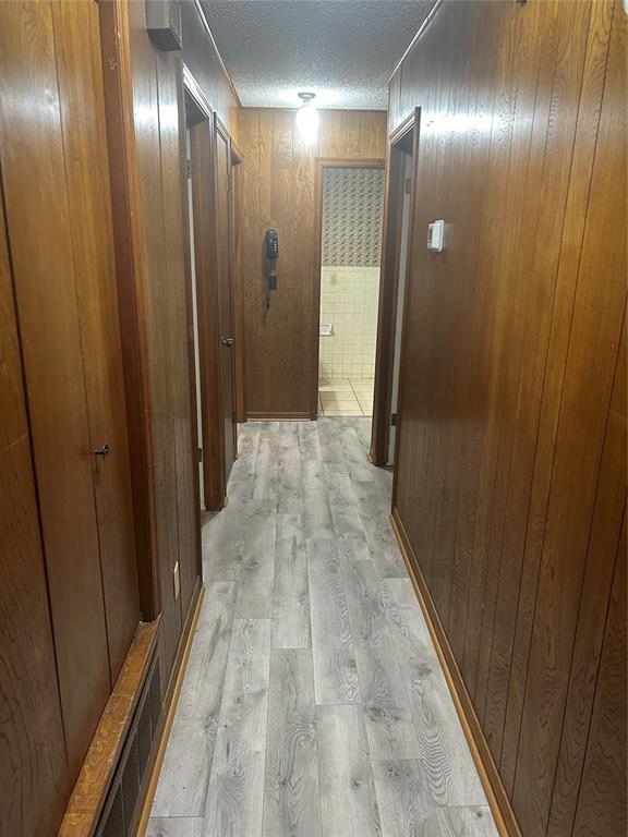 corridor featuring wooden walls, light hardwood / wood-style floors, and a textured ceiling