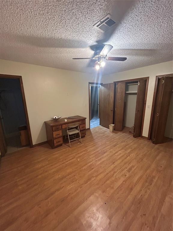 unfurnished bedroom featuring multiple closets, wood-type flooring, and a textured ceiling