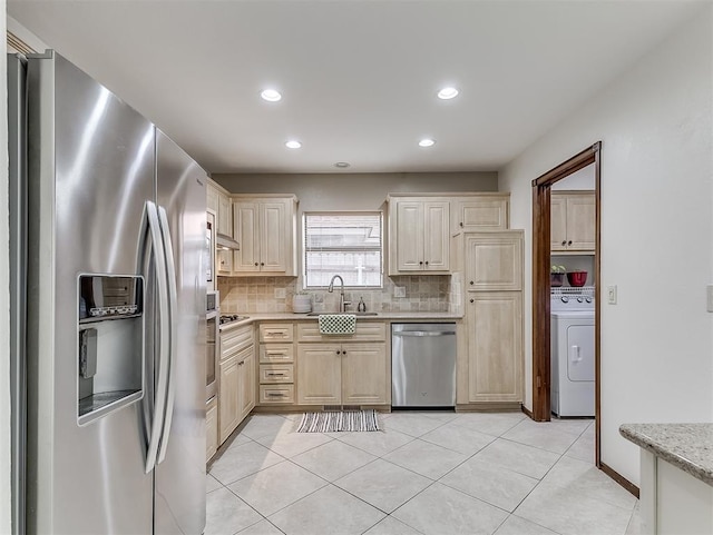 kitchen featuring appliances with stainless steel finishes, washer / clothes dryer, tasteful backsplash, sink, and light stone counters