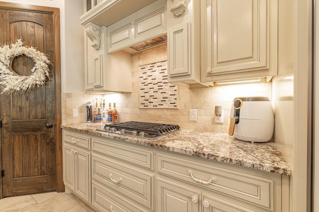 kitchen featuring stainless steel gas stovetop, light stone countertops, cream cabinets, and decorative backsplash