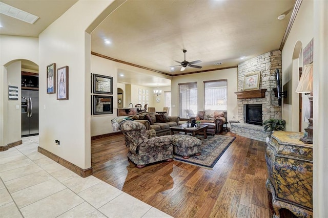 living room featuring ceiling fan with notable chandelier, a fireplace, ornamental molding, and light wood-type flooring