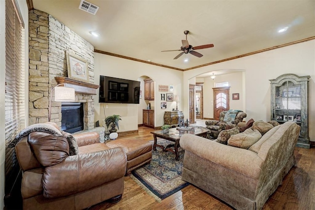 living room featuring hardwood / wood-style flooring, ornamental molding, a stone fireplace, and ceiling fan