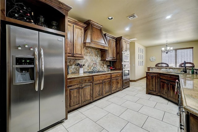 kitchen with tasteful backsplash, custom exhaust hood, hanging light fixtures, a notable chandelier, and stainless steel appliances