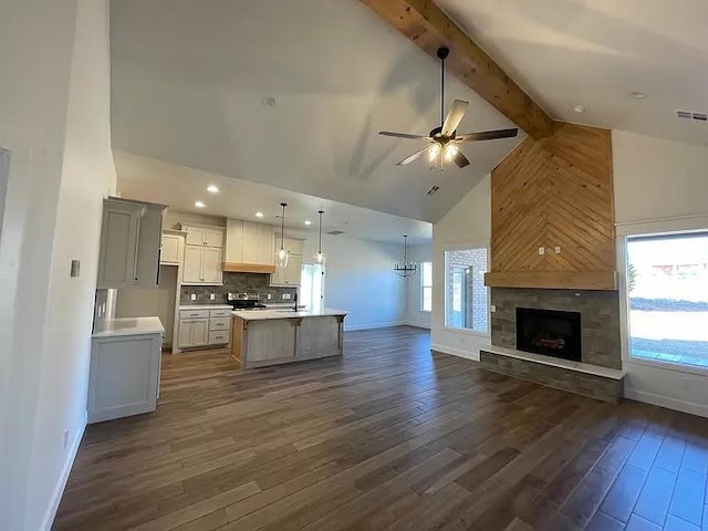 kitchen featuring dark wood-type flooring, decorative light fixtures, stainless steel electric range, a center island with sink, and beam ceiling