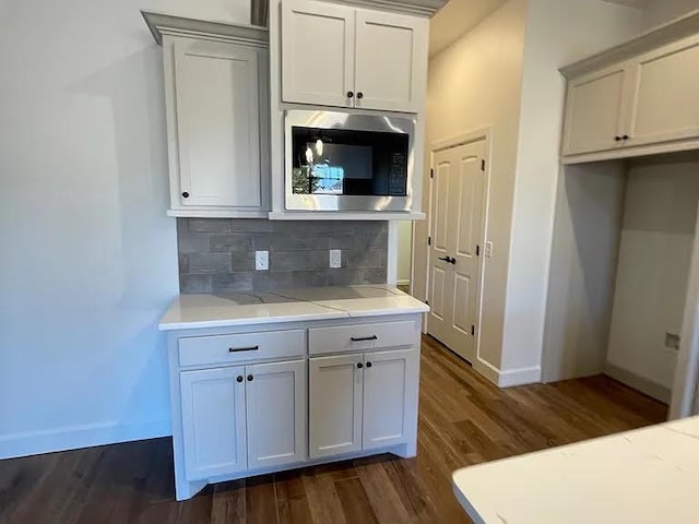 kitchen with stainless steel microwave, white cabinetry, dark hardwood / wood-style flooring, decorative backsplash, and light stone counters