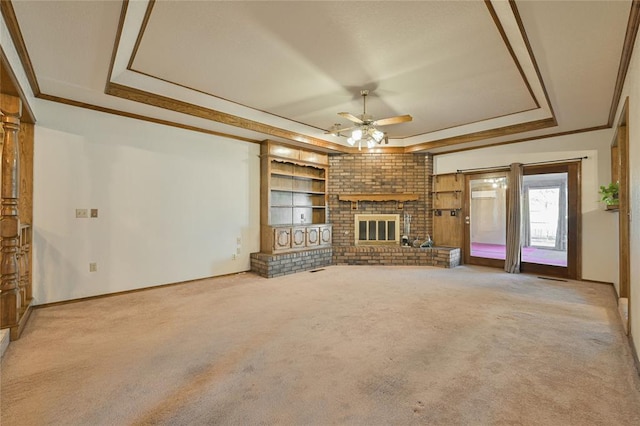 unfurnished living room featuring a raised ceiling, ornamental molding, a brick fireplace, and light colored carpet