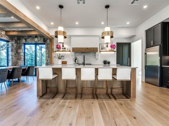 kitchen with hanging light fixtures, a kitchen bar, built in fridge, a large island with sink, and light wood-type flooring